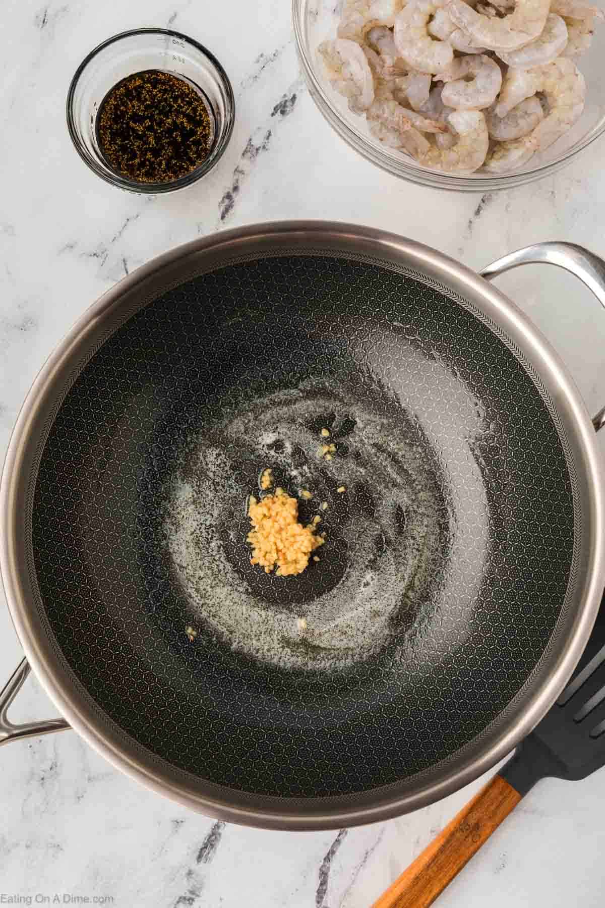 Melted butter with minced garlic in a pan with a bowl of shrimp and sauce on the side