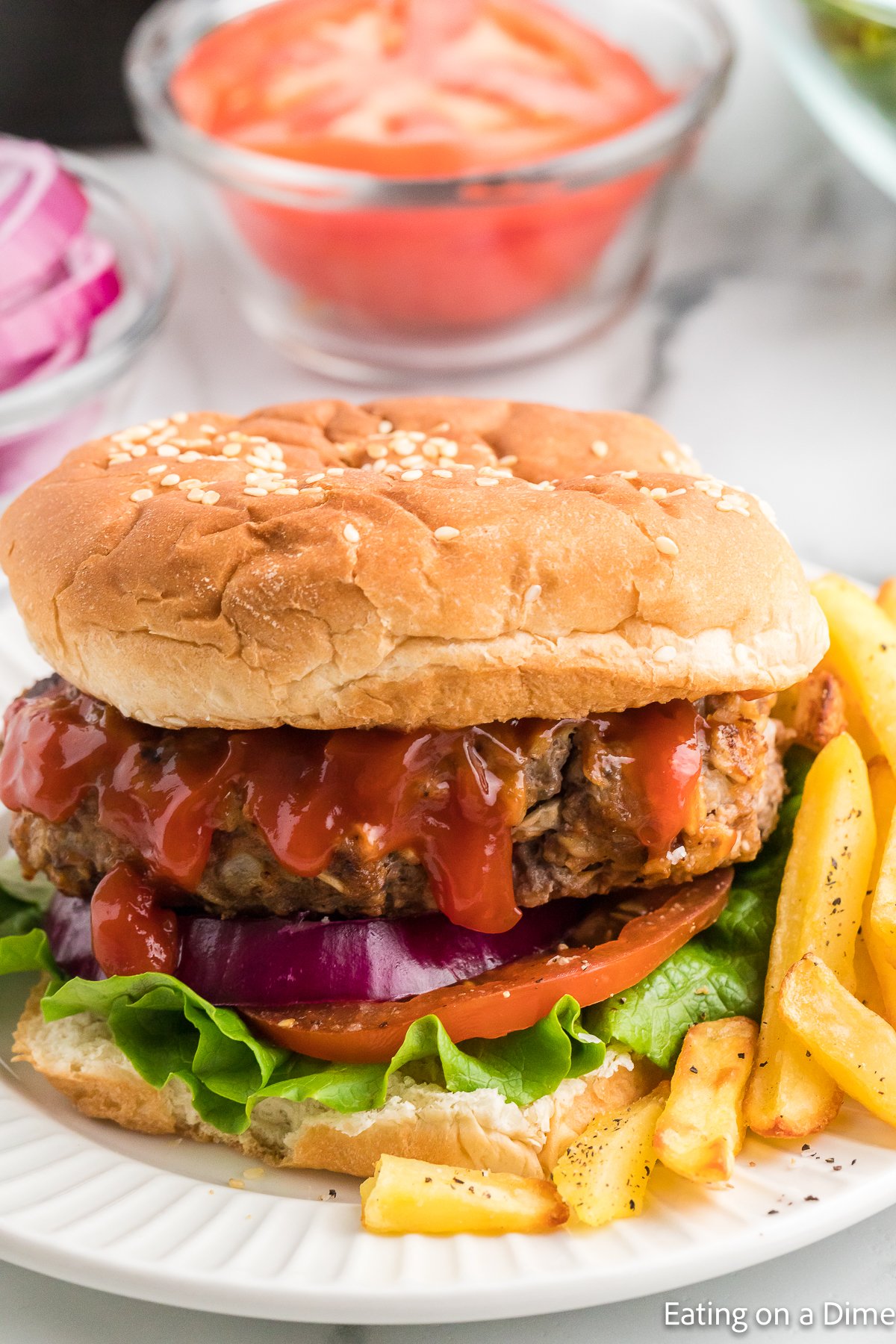 Meatloaf burger on a plate that is layered with red onions, slice tomato and lettuce with a side of French fries