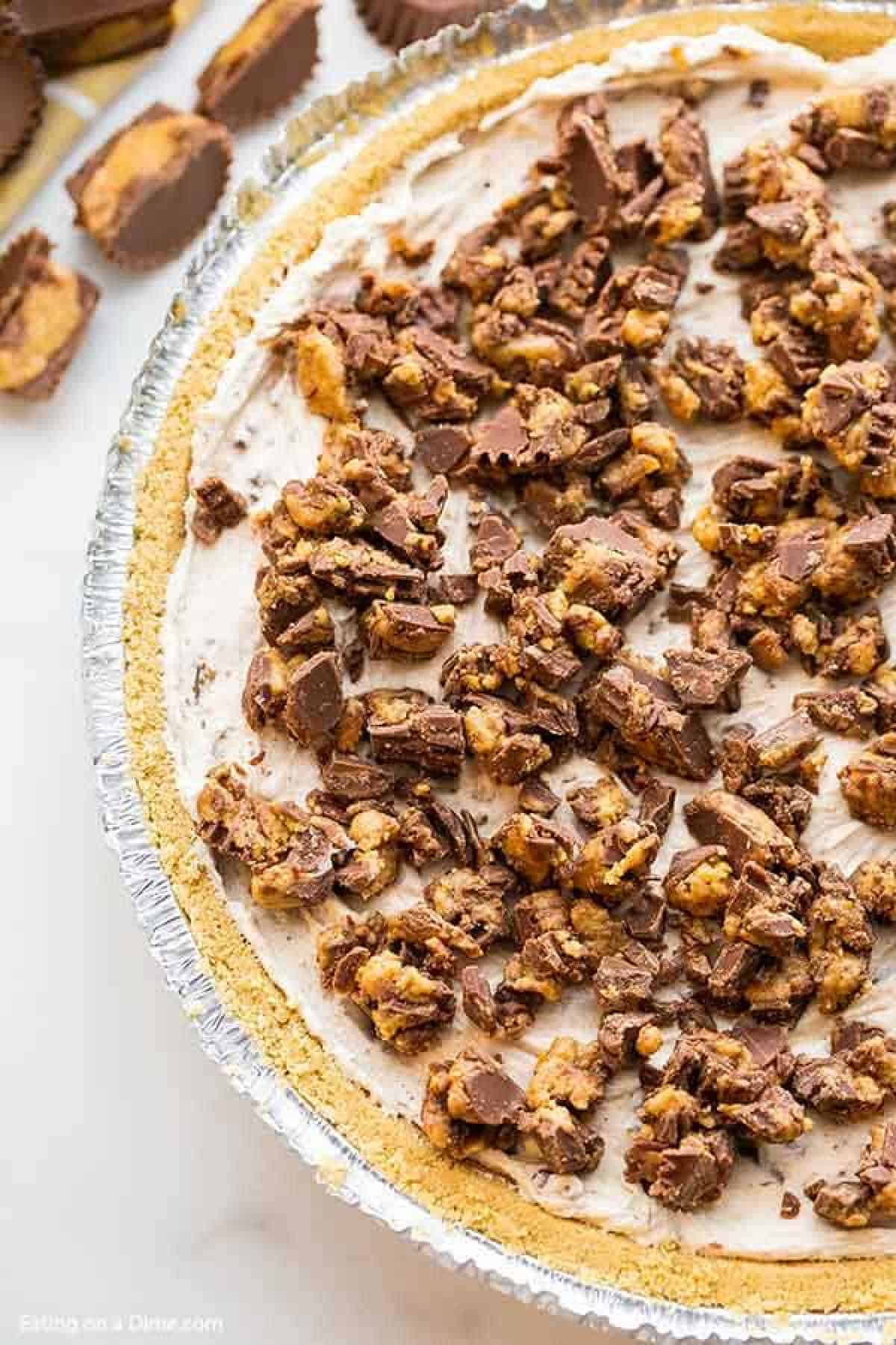 Reese pie in a pie pan topped with crushed Reese's peanut butter cups.