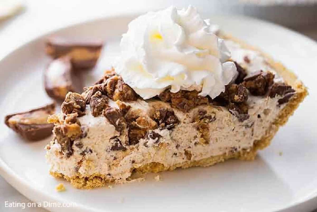 A slice of reese's pie on a white plate topped with whipped cream.