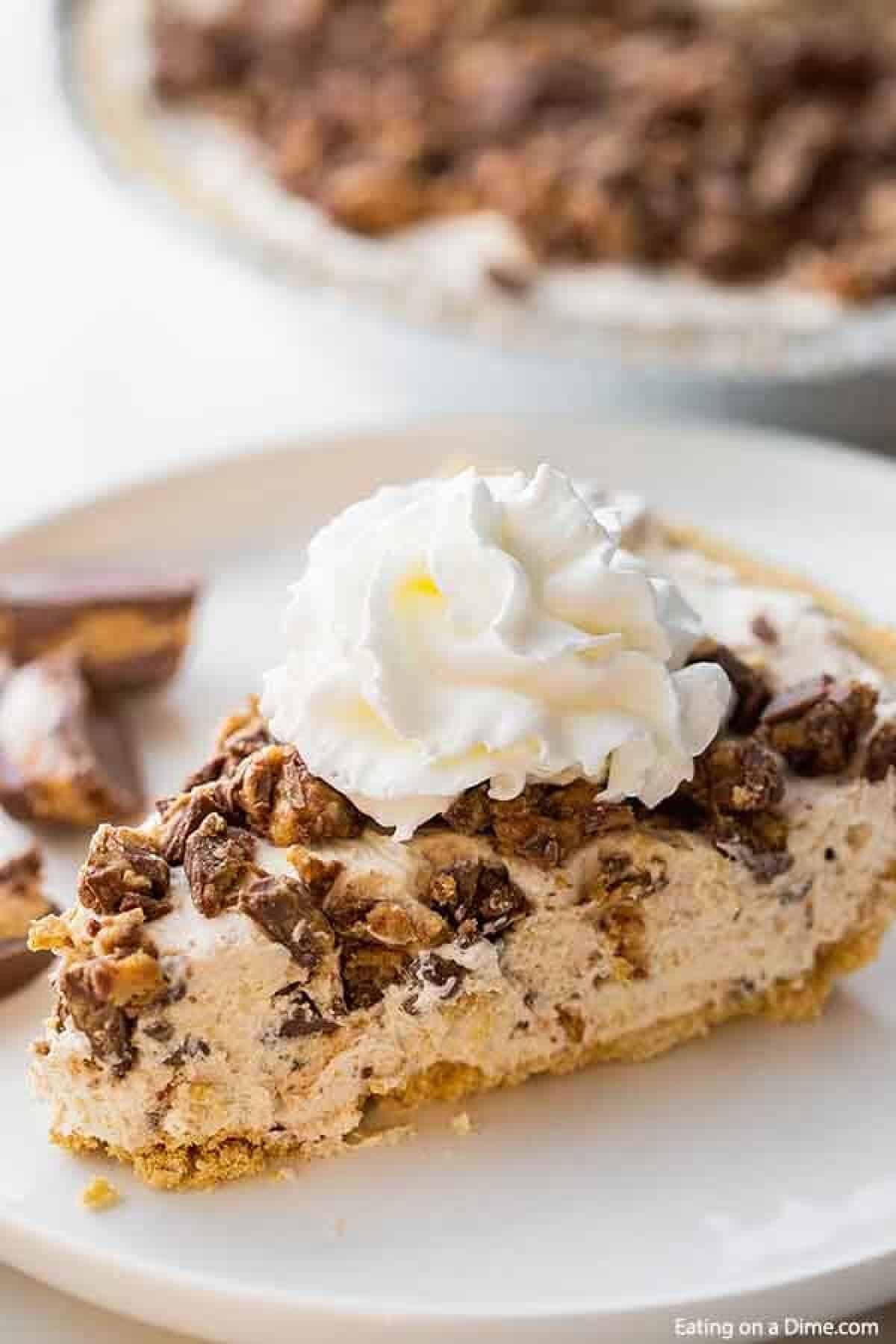 A slice of reese's pie on a white plate topped with whipped cream.