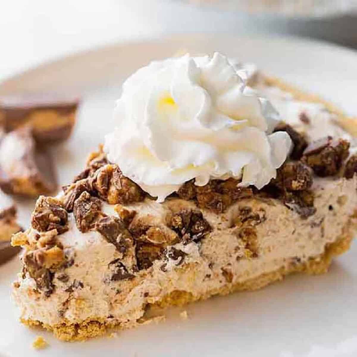 A slice of reese's pie on a white plate topped with whipped cream.