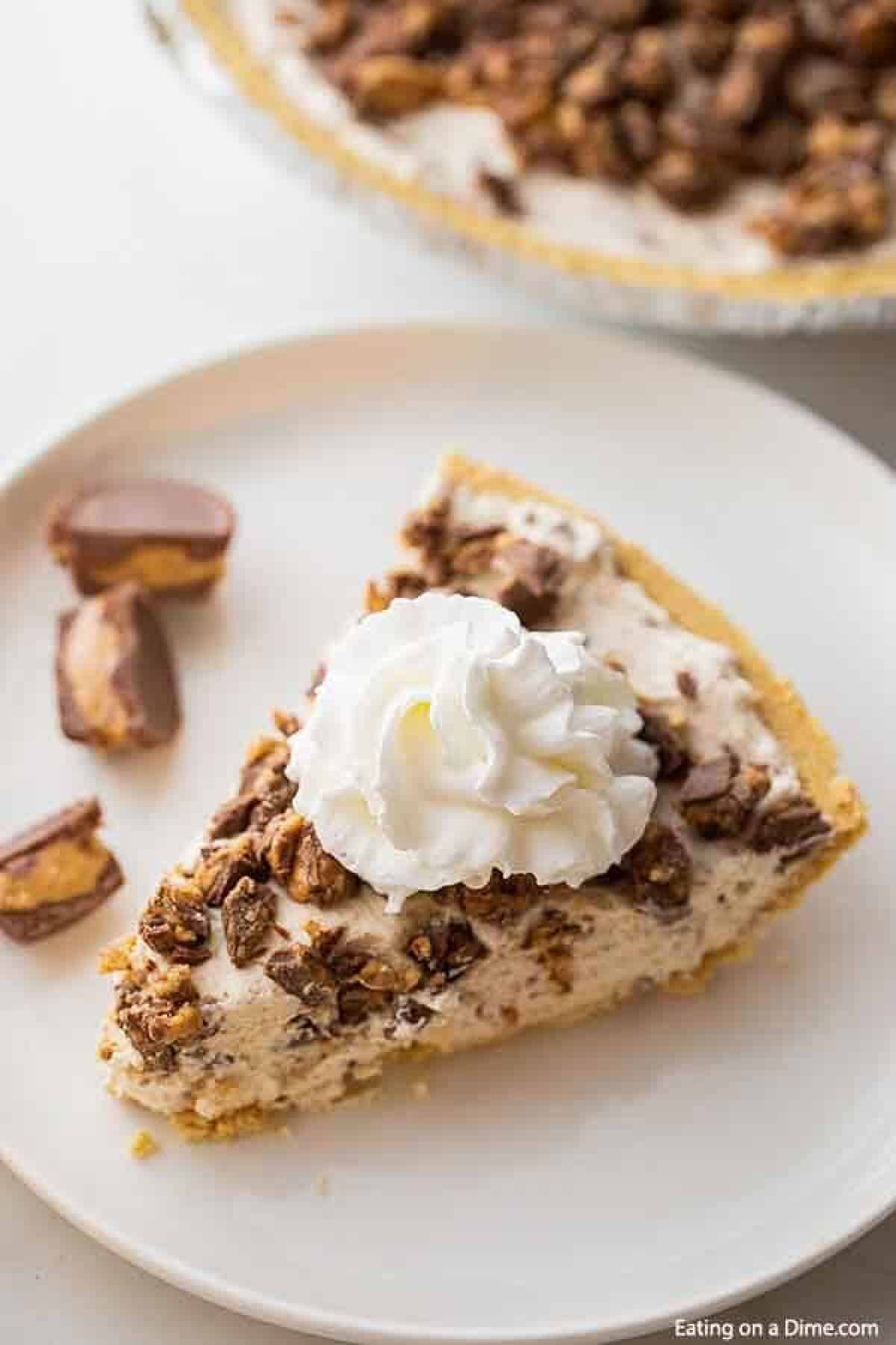 A slice of reese's pie on a white plate topped with whipped cream.