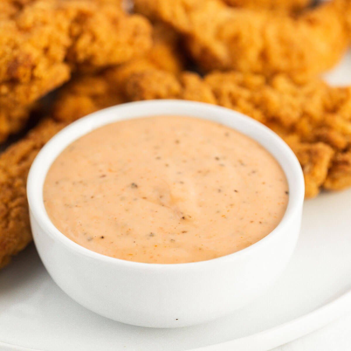 Close up image of chicken fingers and a bowl of chicken dipping sauce