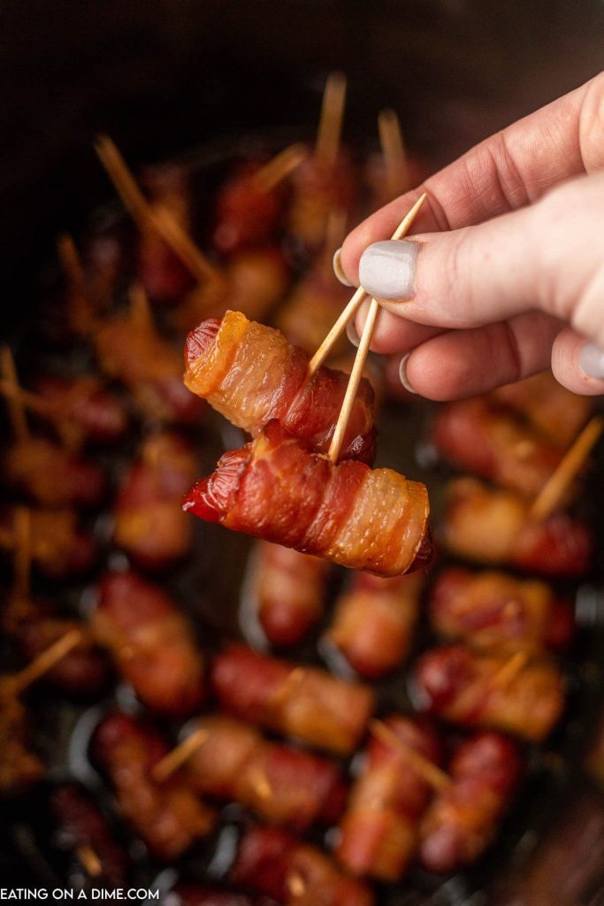 Bacon wrapped lil smokies in a slow cooker with two being held