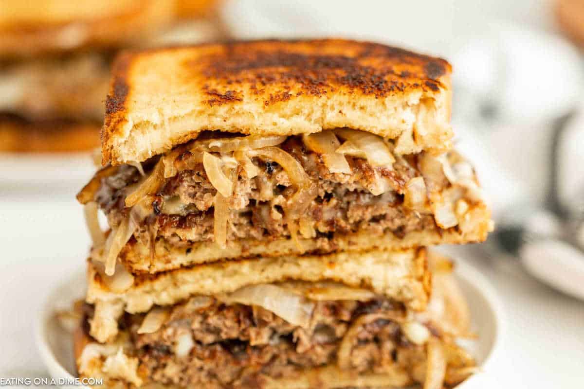 Patty melt cut in half and stacked on a plate.