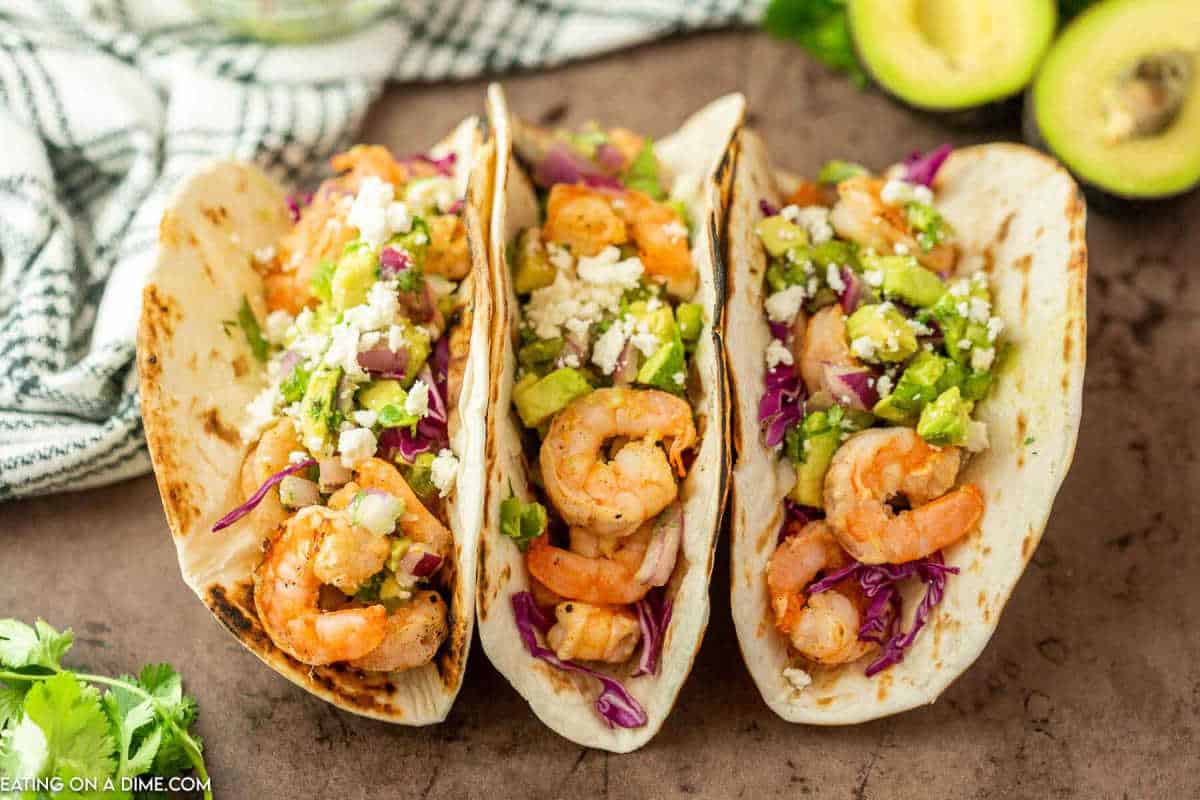 Shrimp tacos topped with red cabbage and diced avocado.