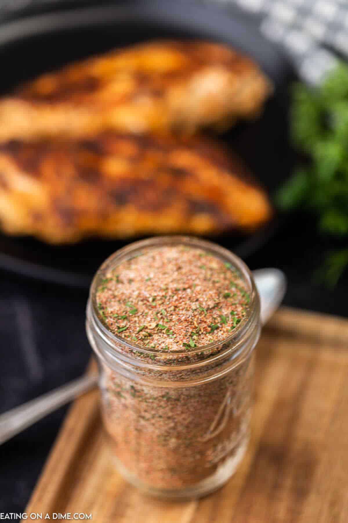 Forget buying blackened spices when you can make this easy Homemade Blackened Seasoning Recipe at home for a lot less. Enjoy Blackened fish, chicken or shrimp! You’ll love this easy cajun spices recipe. It really is the best! #eatingonadime #homemadeseasoningmixes #blackenedseasoningmix Blackened Seasoning Blend in a mason jar with grilled chicken on a plate in the background