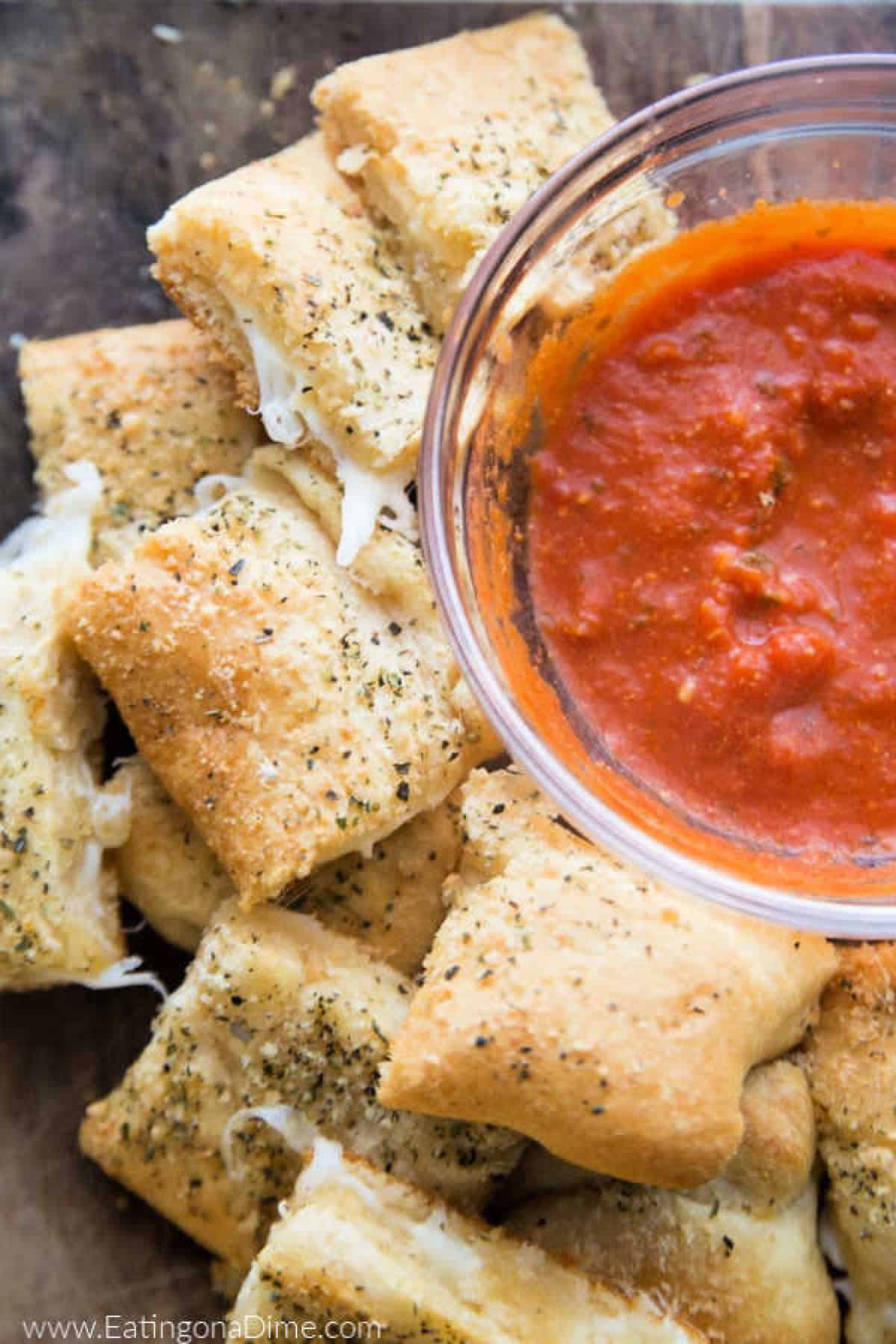 You just have to make this Stuffed Cheesy Bread Recipe with crescent rolls. This is the best cheesy bread and it only takes 15 minutes to make! Try this easy bread recipe. #eatingonadime #appetizerrecipes #breadrecipes Cheesy bread stacked with a side of marinara sauce