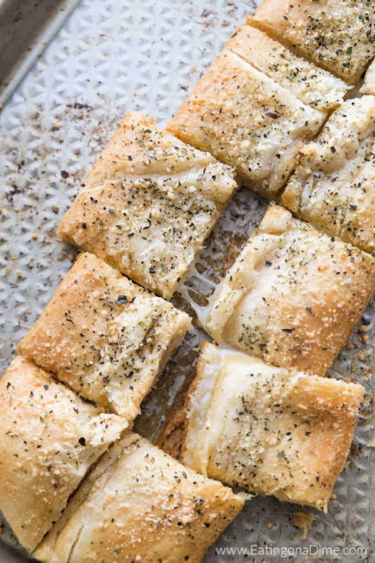 You just have to make this Stuffed Cheesy Bread Recipe with crescent rolls. This is the best cheesy bread and it only takes 15 minutes to make! Try this easy bread recipe. #eatingonadime #appetizerrecipes #breadrecipes Cheesy Bread on a baking sheet