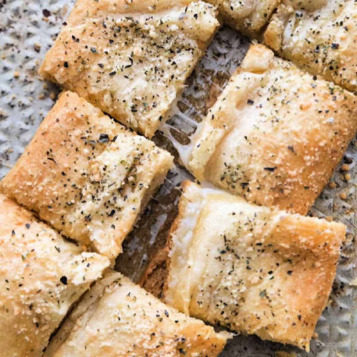 You just have to make this Stuffed Cheesy Bread Recipe with crescent rolls. This is the best cheesy bread and it only takes 15 minutes to make! Try this easy bread recipe. #eatingonadime #appetizerrecipes #breadrecipes Cheesy bread on a baking sheet