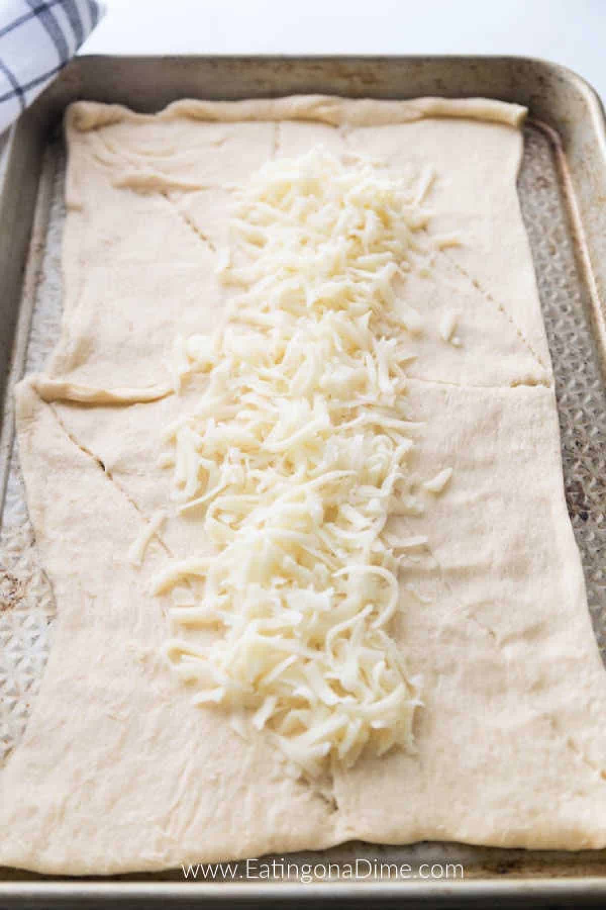 You just have to make this Stuffed Cheesy Bread Recipe with crescent rolls. This is the best cheesy bread and it only takes 15 minutes to make! Try this easy bread recipe. #eatingonadime #appetizerrecipes #breadrecipes Topping the bread dough with cheese