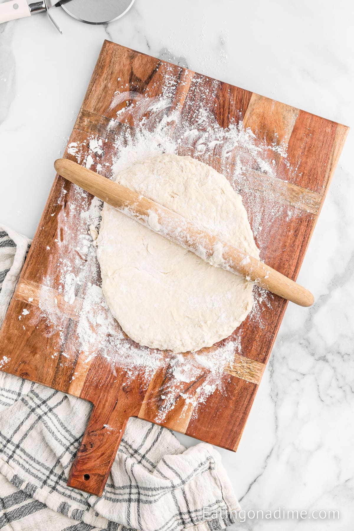 Dough in a cutting board with flour and a rolling pin