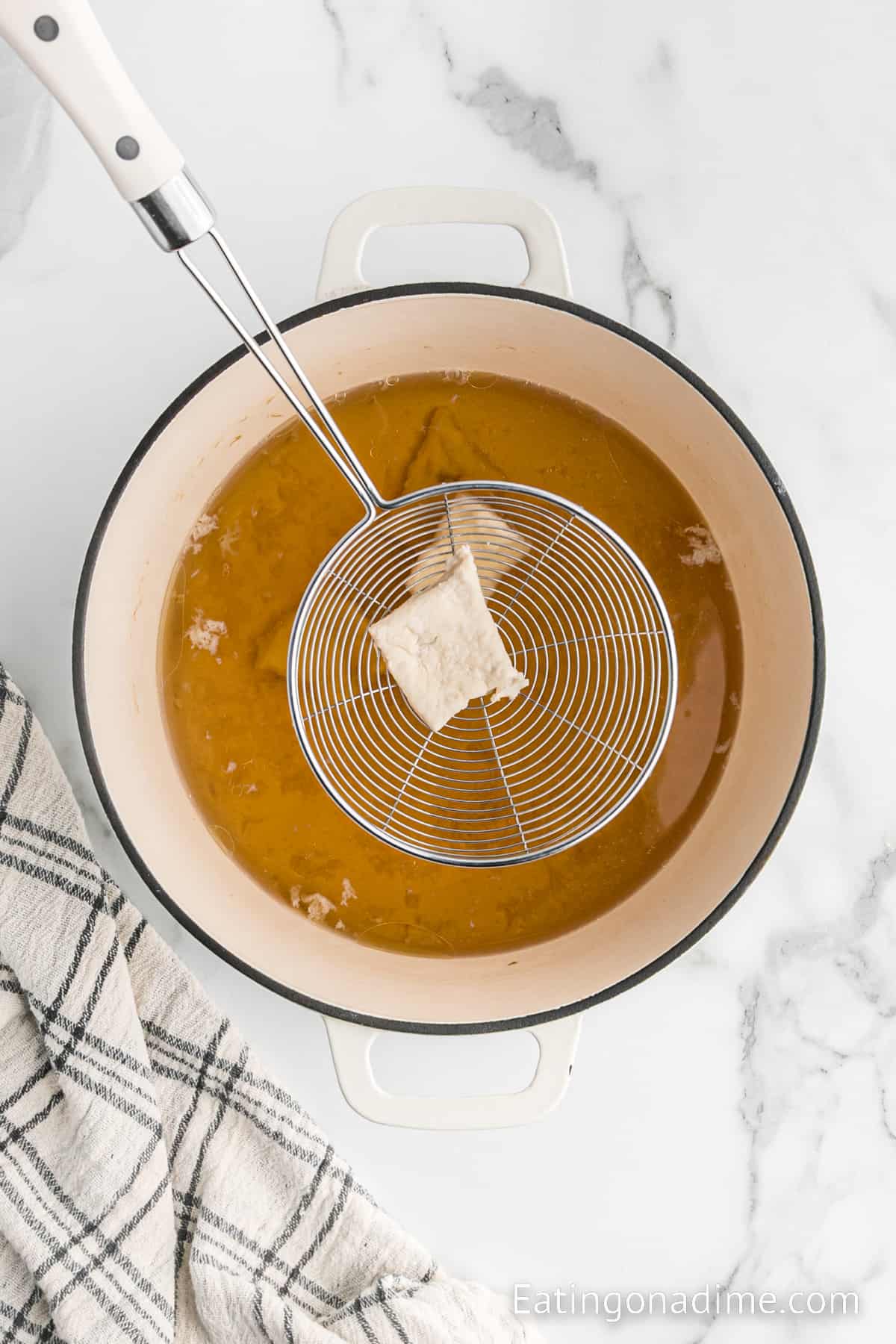 Large pot with oil with pieces of dough on a spatula