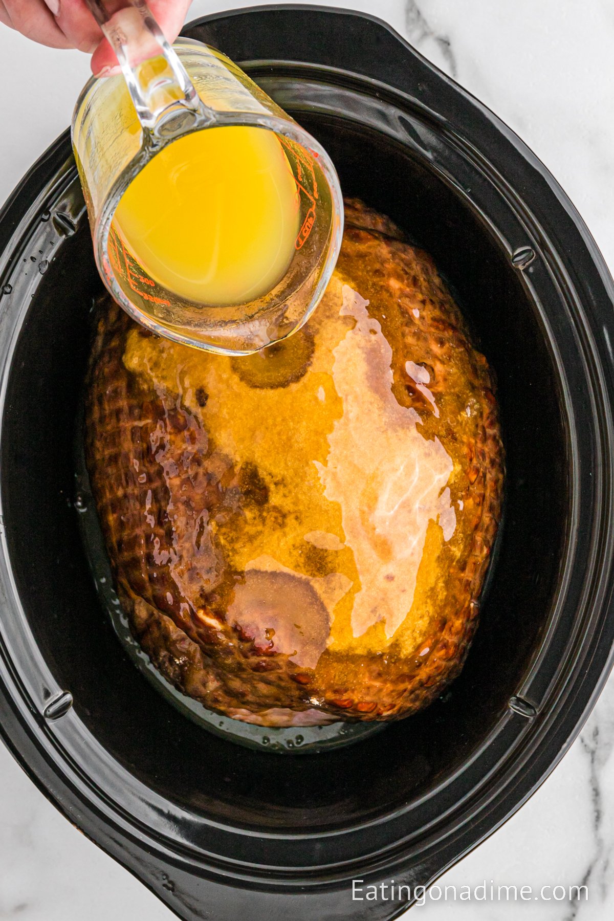 Pouring pineapple juice over the ham in the slow cooker 