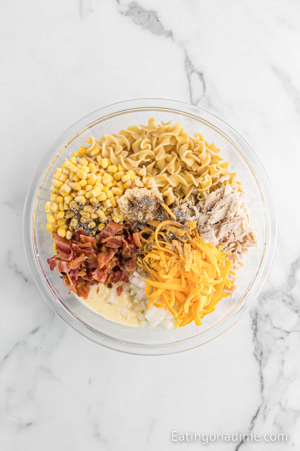 Chopped bacon, shredded chicken, shredded cheese, egg noodles, corn, seasoning mixed together in a bowl