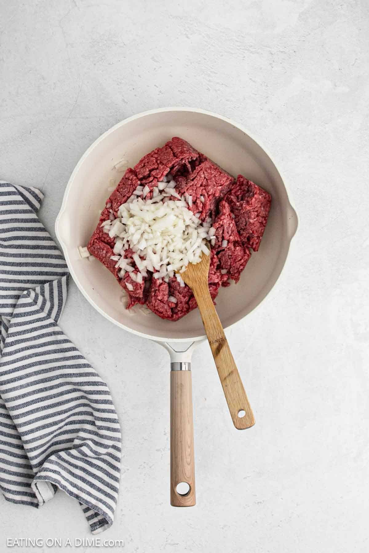 Cooking ground beef in a skillet topped with diced onions.