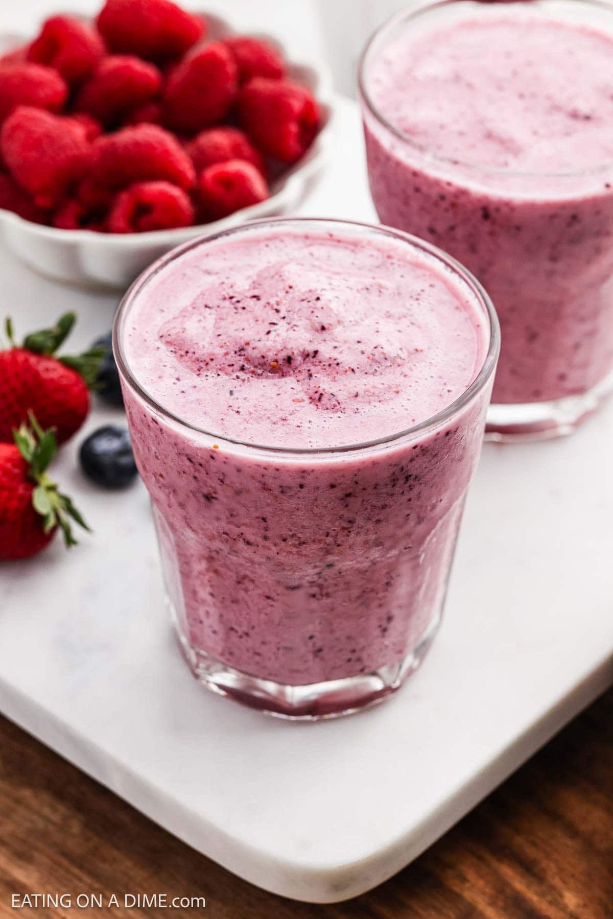 Smoothie in clear glasses with fresh raspberries, strawberries and blueberries nearby.