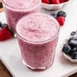 2 Fruit Smoothies on a marble counter with fresh blueberries and strawberries on the side.