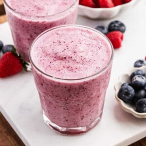 2 Fruit Smoothies on a marble counter with fresh blueberries and strawberries on the side.