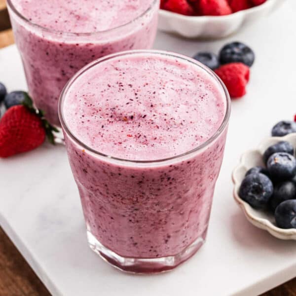 2 Fruit Smoothies on a marble counter with fresh blueberries and strawberries on the side.