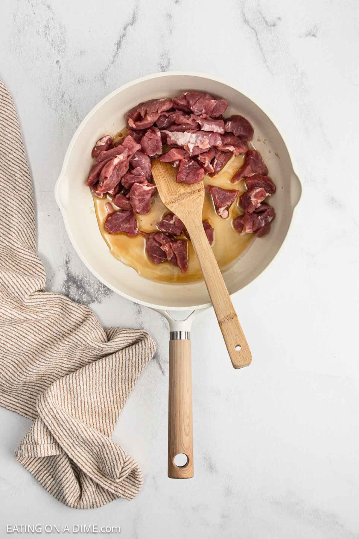 Cooking the diced pork in a large skillet with a wooden spoon and oil.