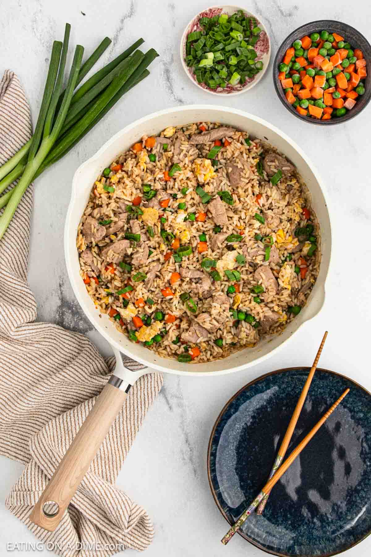 Pork, rice, peas, carrots and topped with greens onions in a skillet. With a small bowl of frozen peas and carrots and green onions.