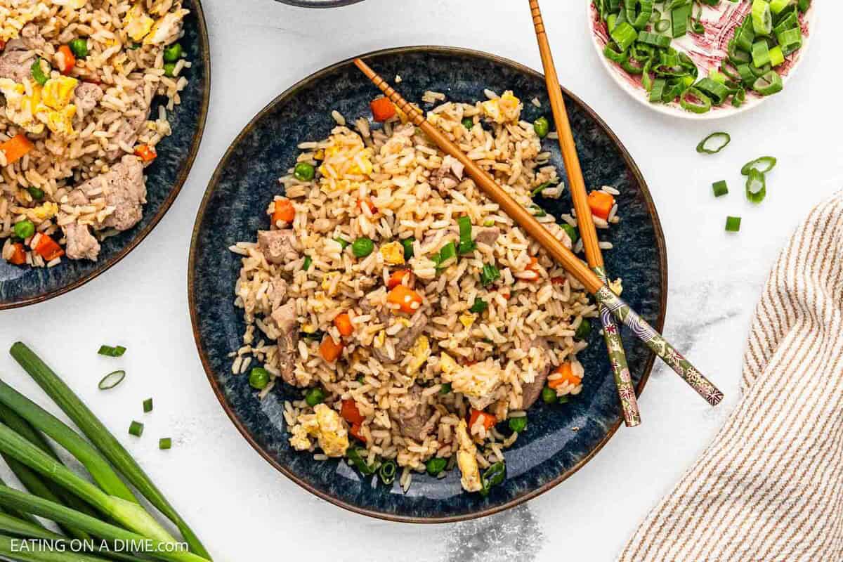 Pork Fried Rice on a blue plate with chopsticks and a small plate of green onions on the side.