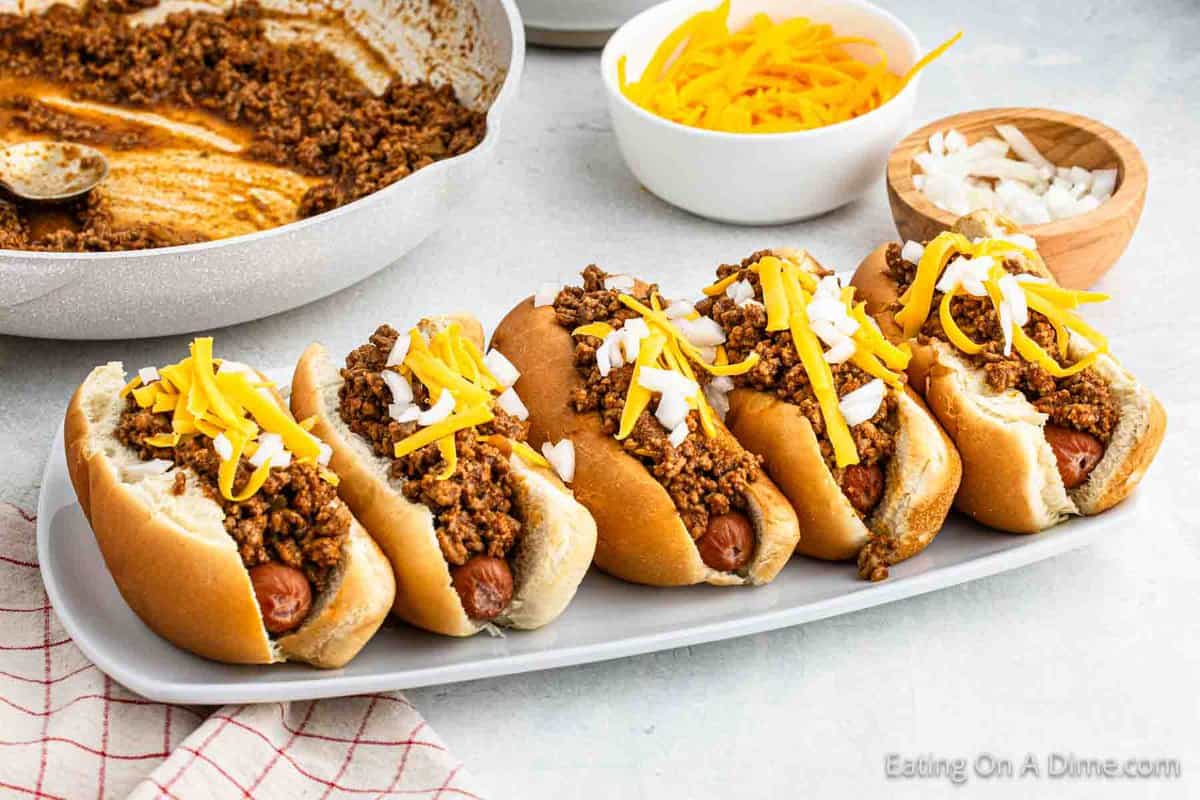 Hot dogs on a platter topped with chili, diced onions and shredded cheese