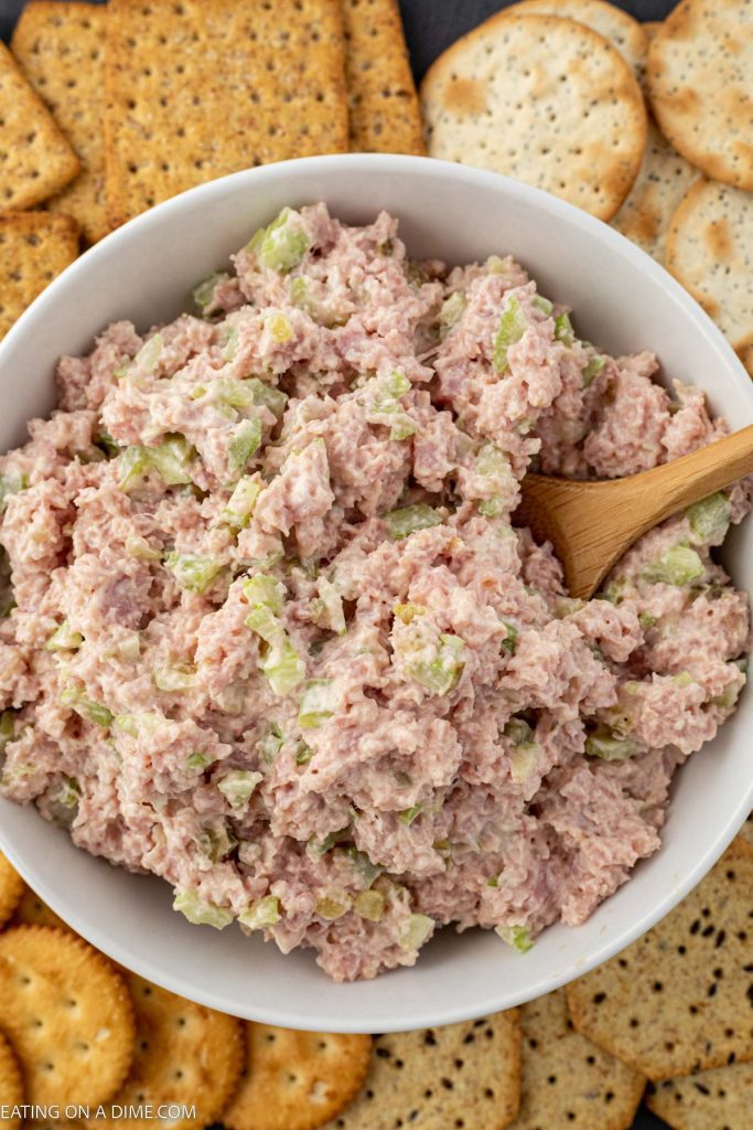 Bowl of ham salad with a wooden spoon and a side of crackers