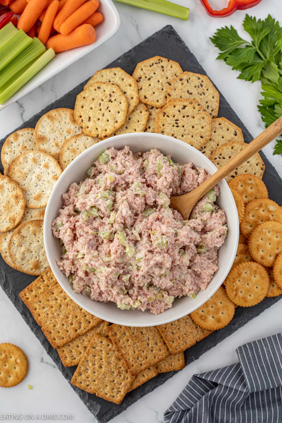 Bowl of ham salad with a wooden spoon and a side of crackers