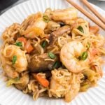 A plate of shrimp yakisoba lo mein with noodles, shrimp, carrots, mushrooms, and green onions, served with chopsticks on the side.