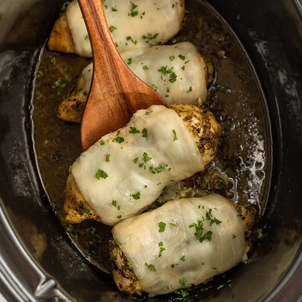 Pesto Chicken in the slow cooker with a wooden spoon