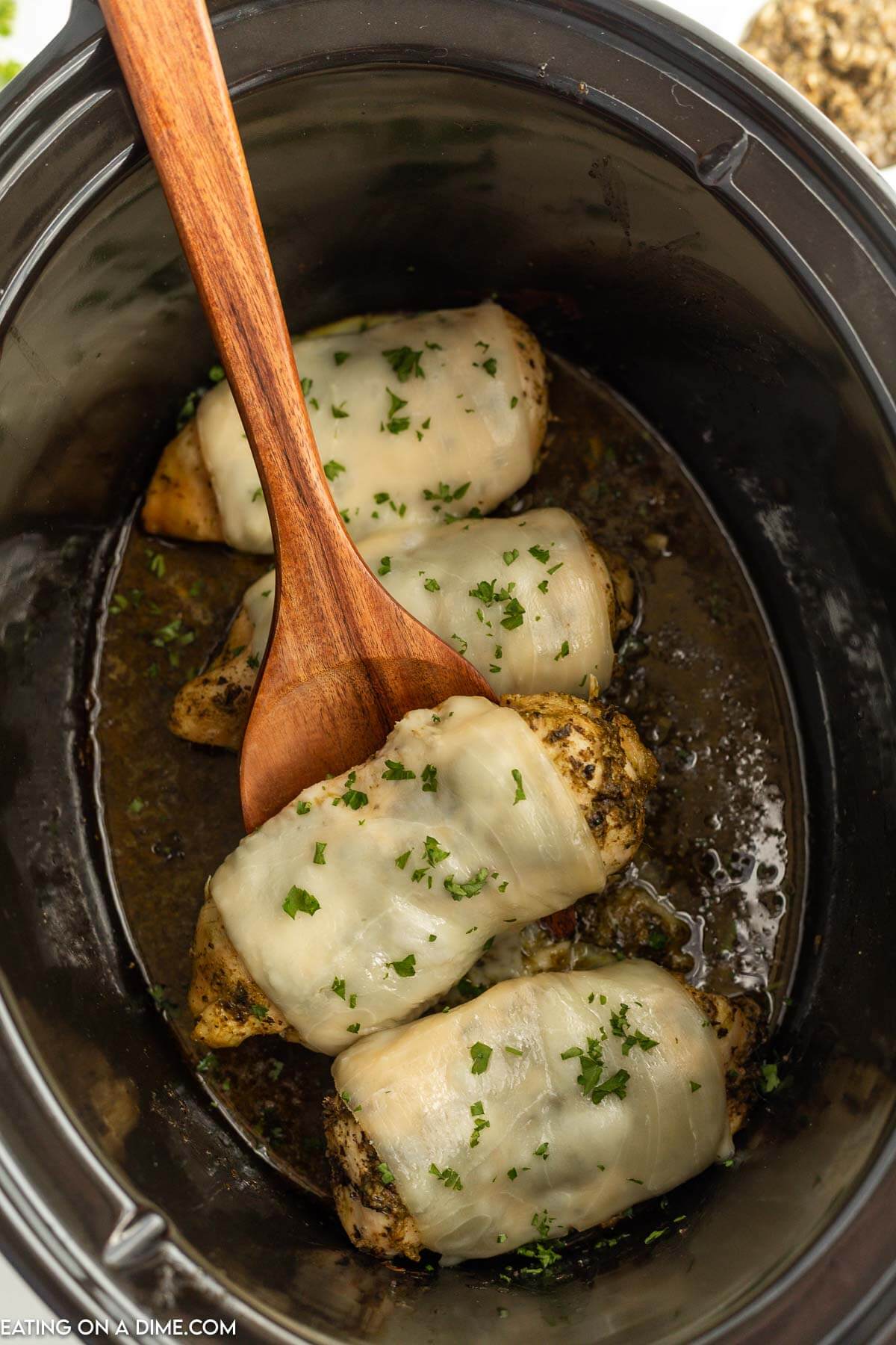 Pesto Chicken in the slow cooker with a wooden spoon