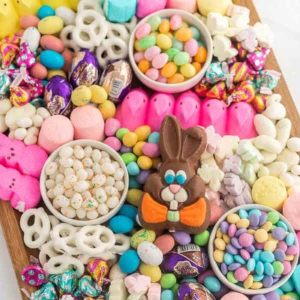 A colorful Easter Candy Charcuterie Board featuring jelly beans, chocolate eggs, pastel marshmallow Peeps, yogurt-covered pretzels, candy-coated chocolates, and a chocolate bunny centerpiece on a wooden tray.