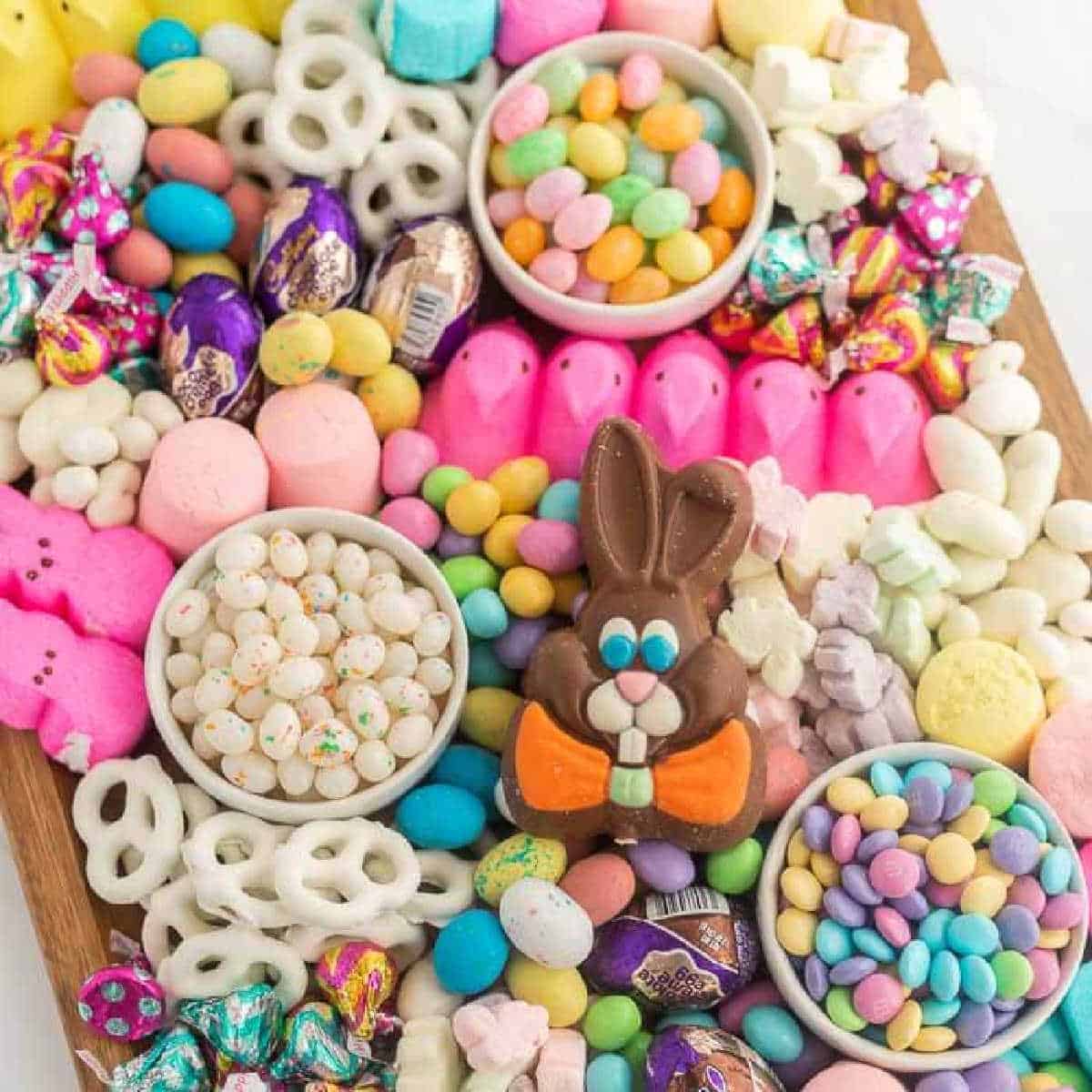 A colorful Easter Candy Charcuterie Board featuring jelly beans, chocolate eggs, pastel marshmallow Peeps, yogurt-covered pretzels, candy-coated chocolates, and a chocolate bunny centerpiece on a wooden tray.
