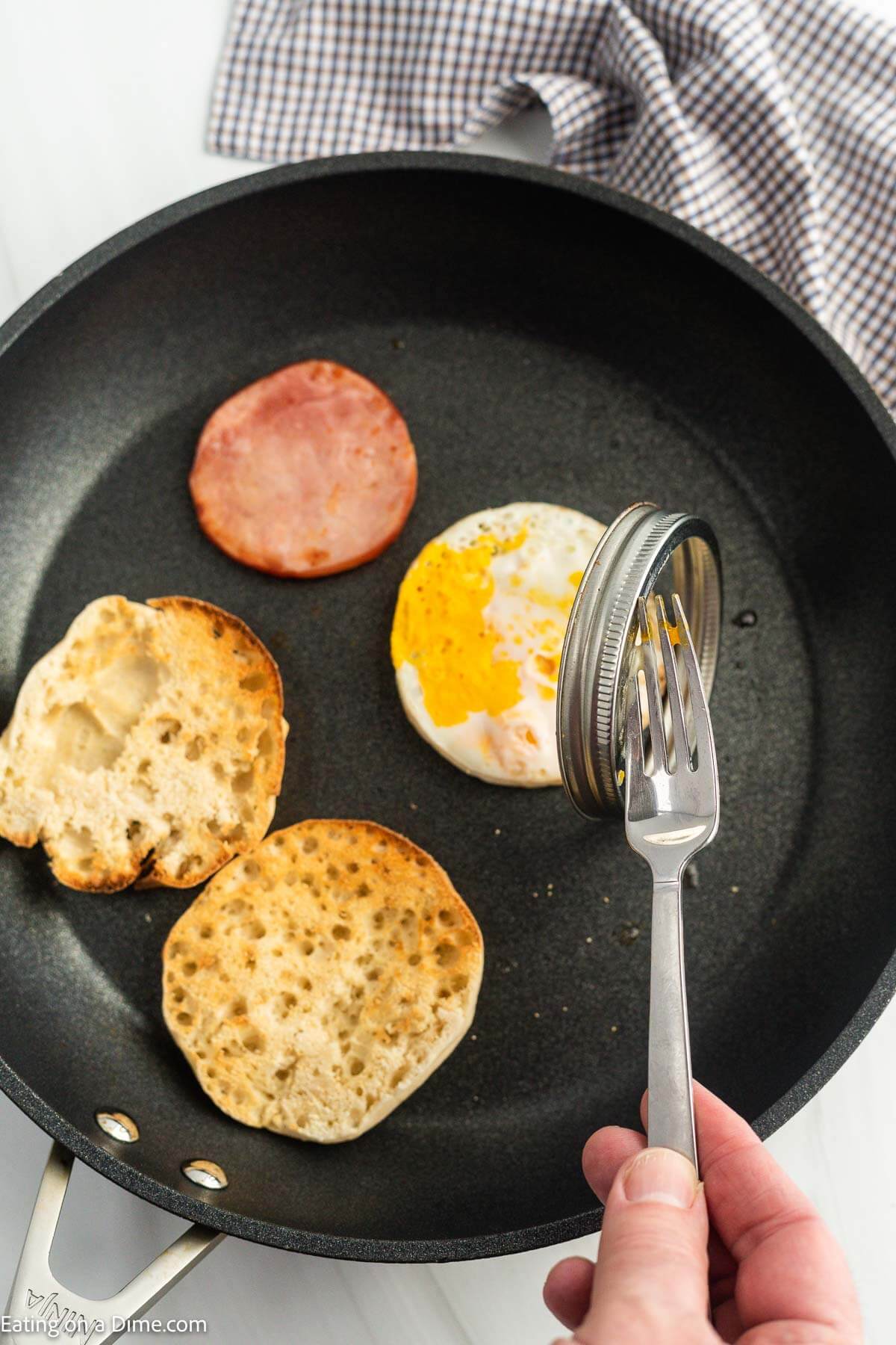 Taking the cooked egg out of the mason jar lid with the toasted McMuffin and cooked canadian bacon in the skillet.