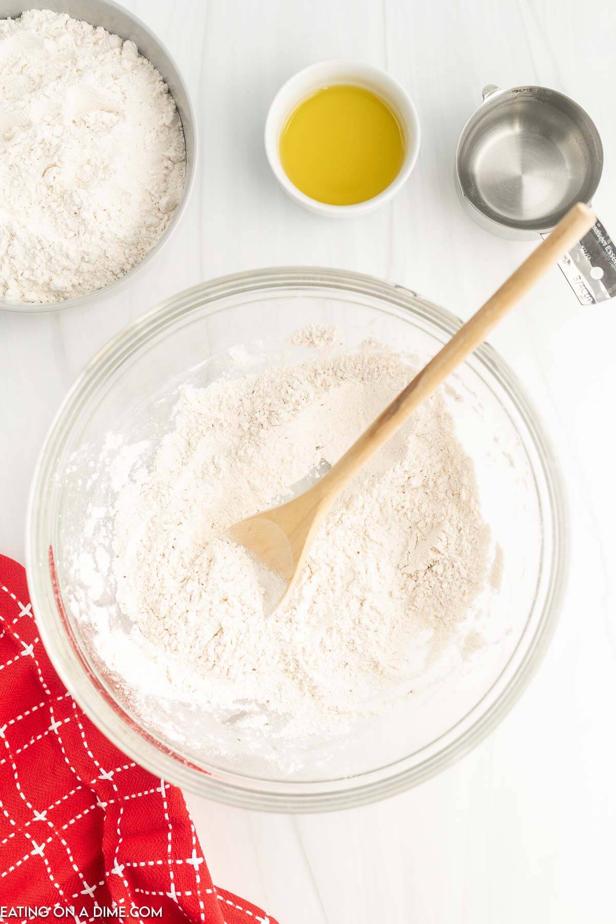 Combining dry ingredients in a bowl with a wooden spoon with a bowl of flour, oil and water on the side