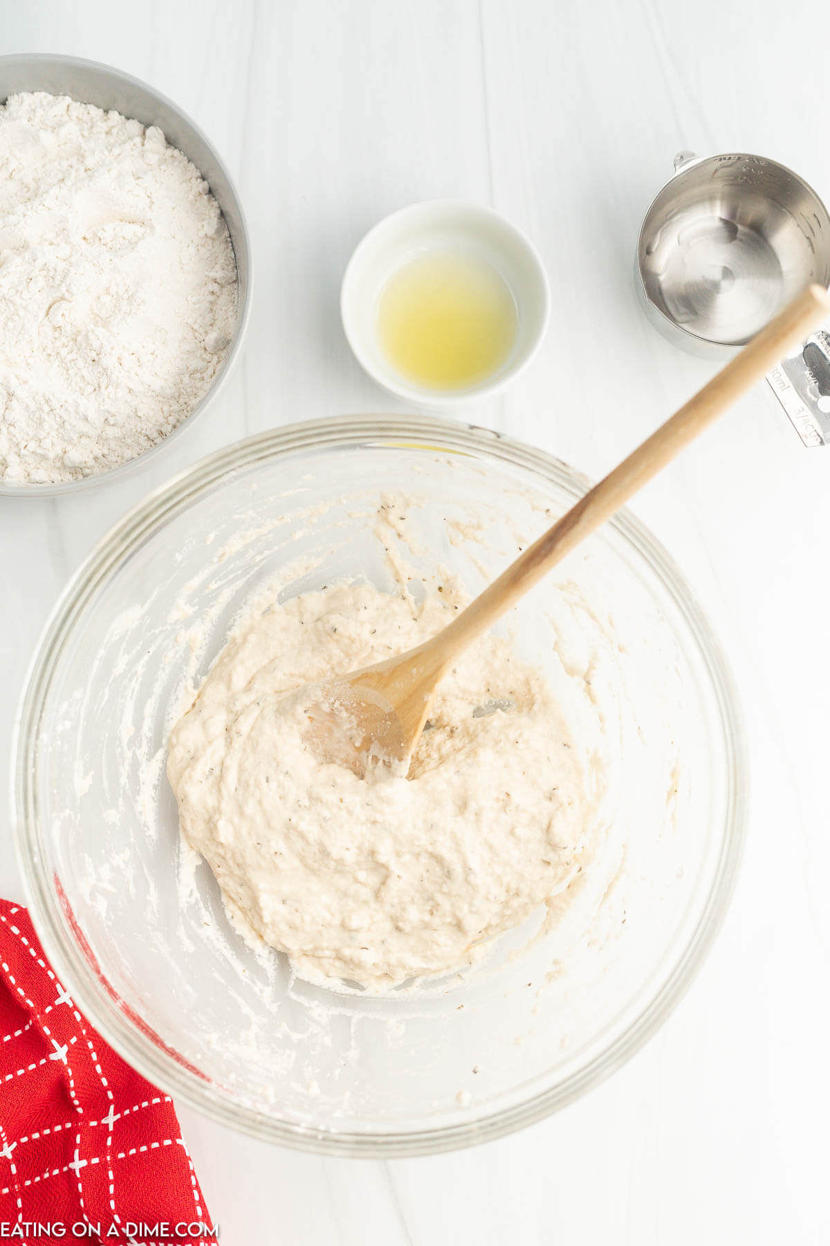 Combining the dough in a bowl with a wooden spoon with a small bowl of flour, oil and water on the side