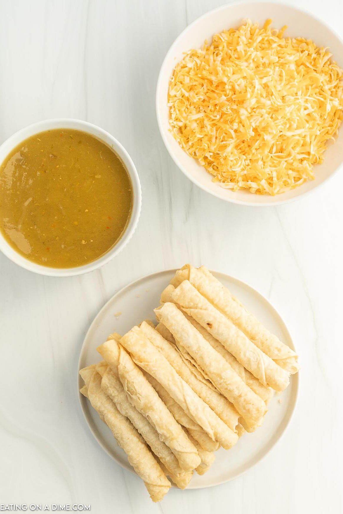 Taquitos on a plate with green enchilada sauce with cheese