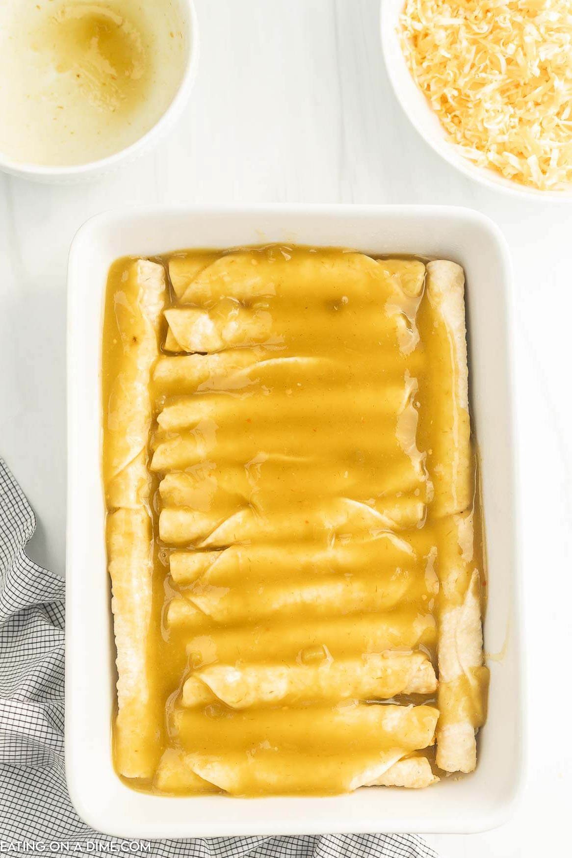 Taquitos in a baking dish and green enchilada sauce poured over the top