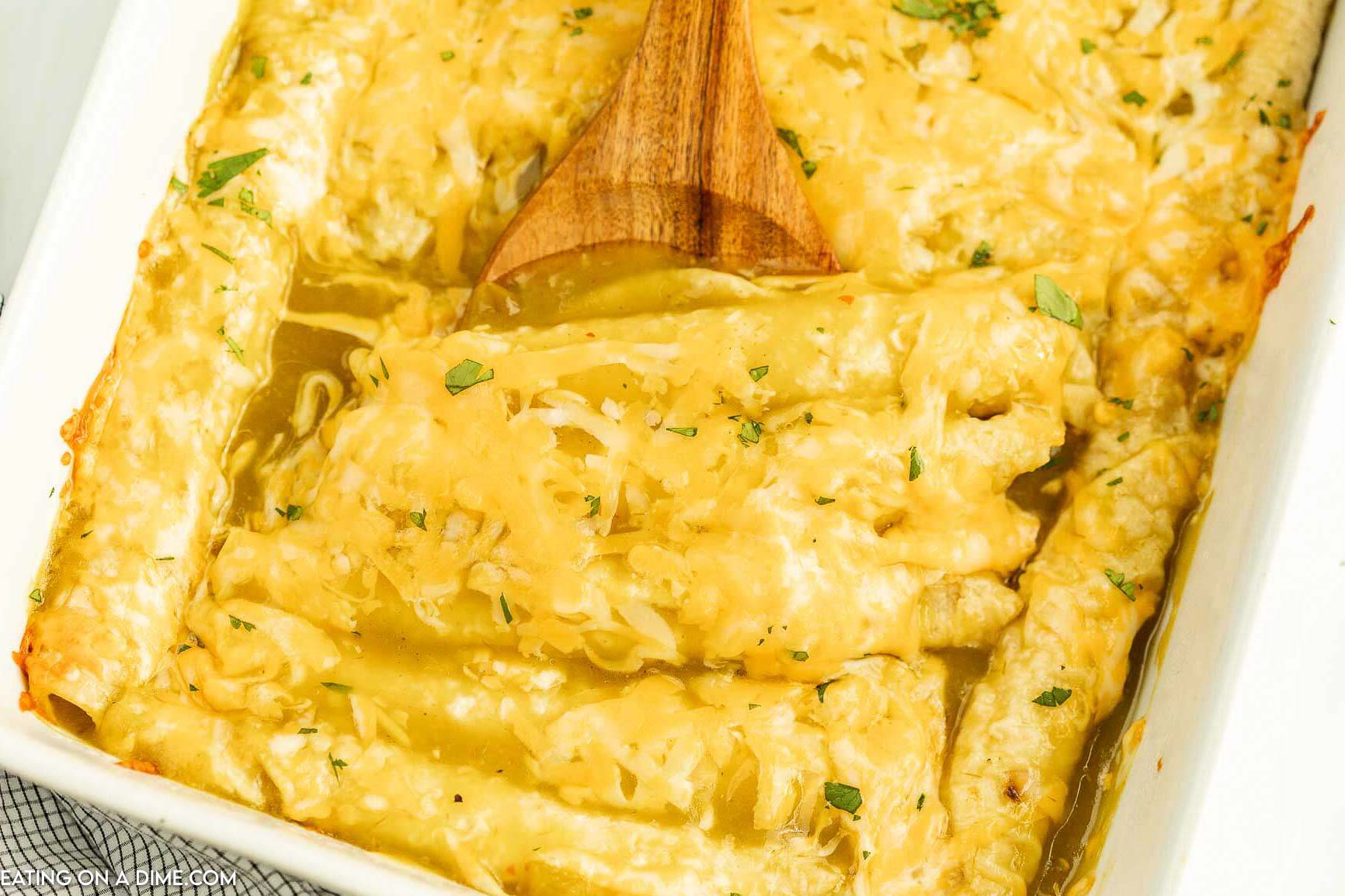 enchiladas in a baking dish with a wooden spoon