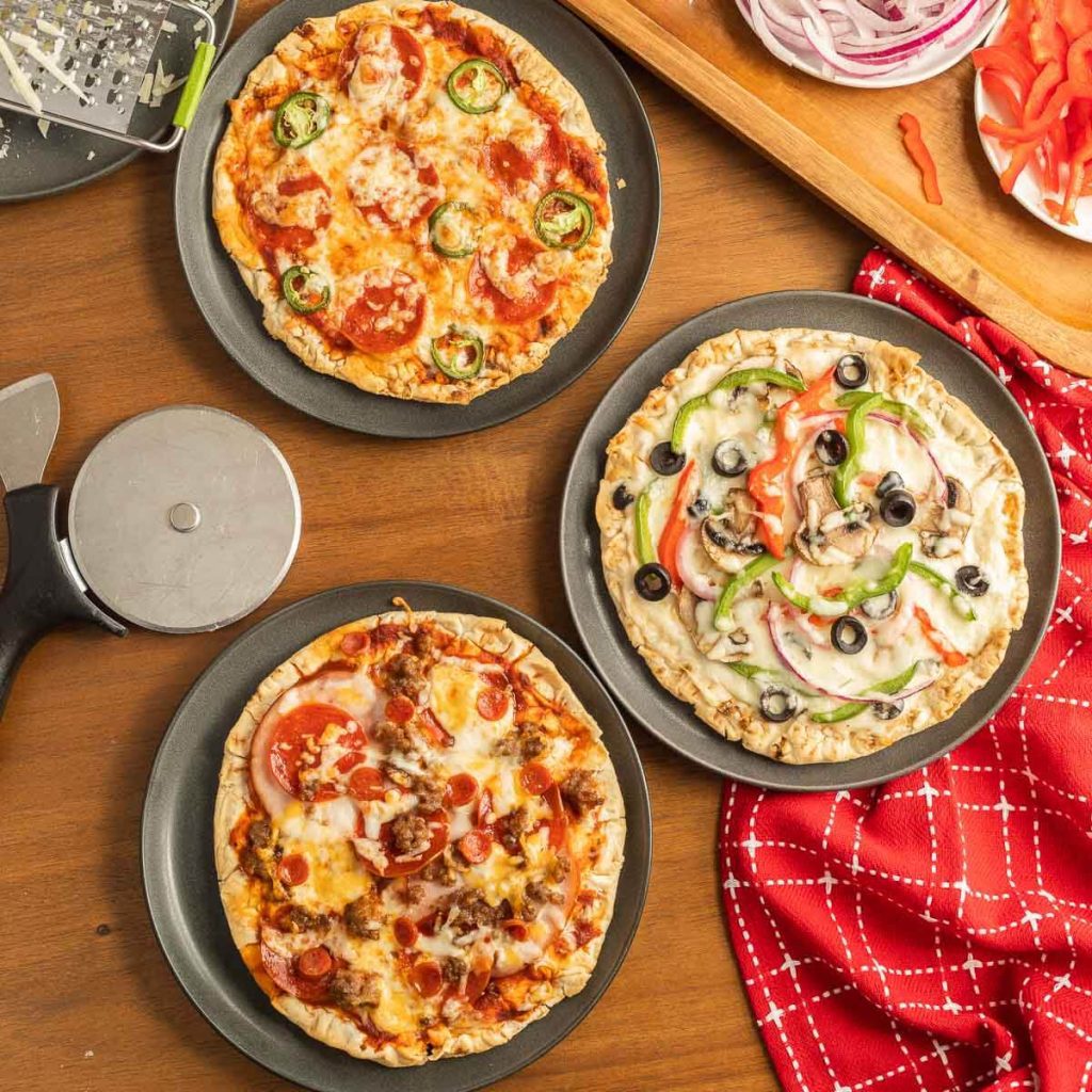 Pizzas on plates with a bowls of different pizza toppings