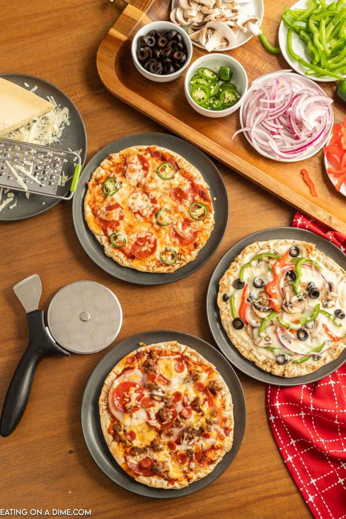 Pizzas on plates with a bowls of different pizza toppings