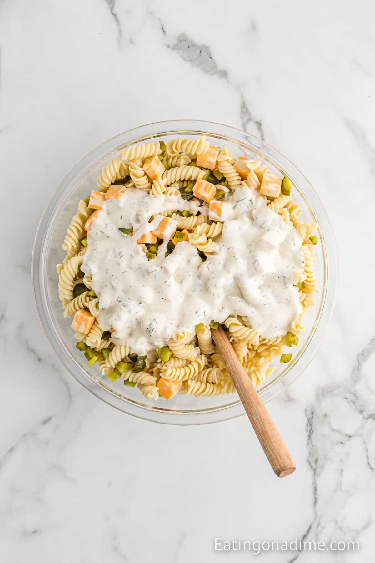 Pouring the prepared dressing over the topped of the pasta, chopped pickles and cubed cheese with a wooden spoon