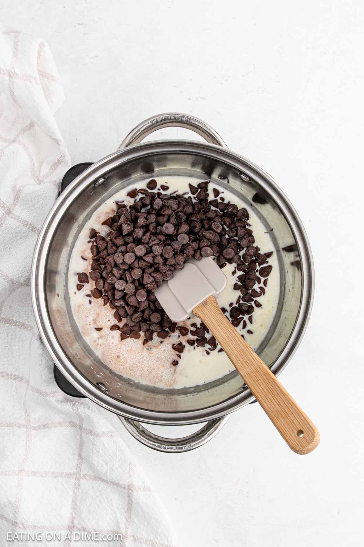 Heavy Cream poured into large pot with chocolate chips with a spatula