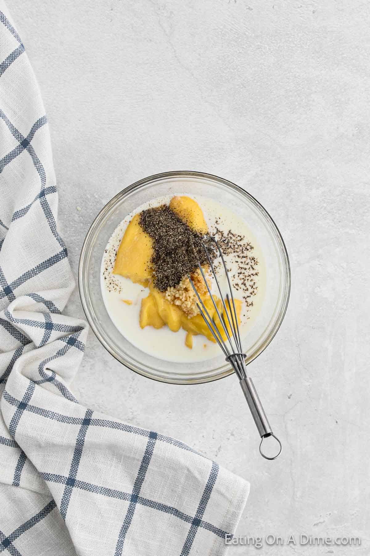 Combining, chicken soup, milk, and seasoning in a bowl with a whisk