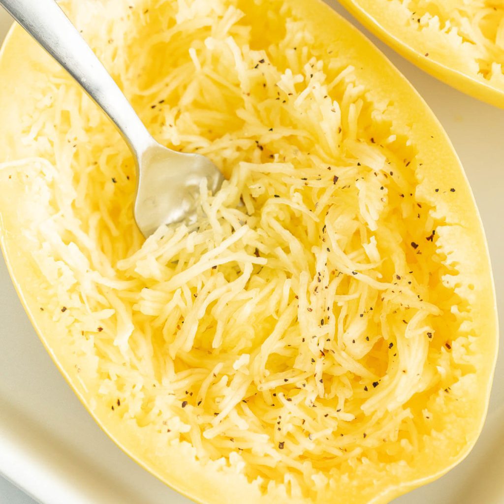 Cooked spaghetti squash in a baking dish with a fork shredding the squash