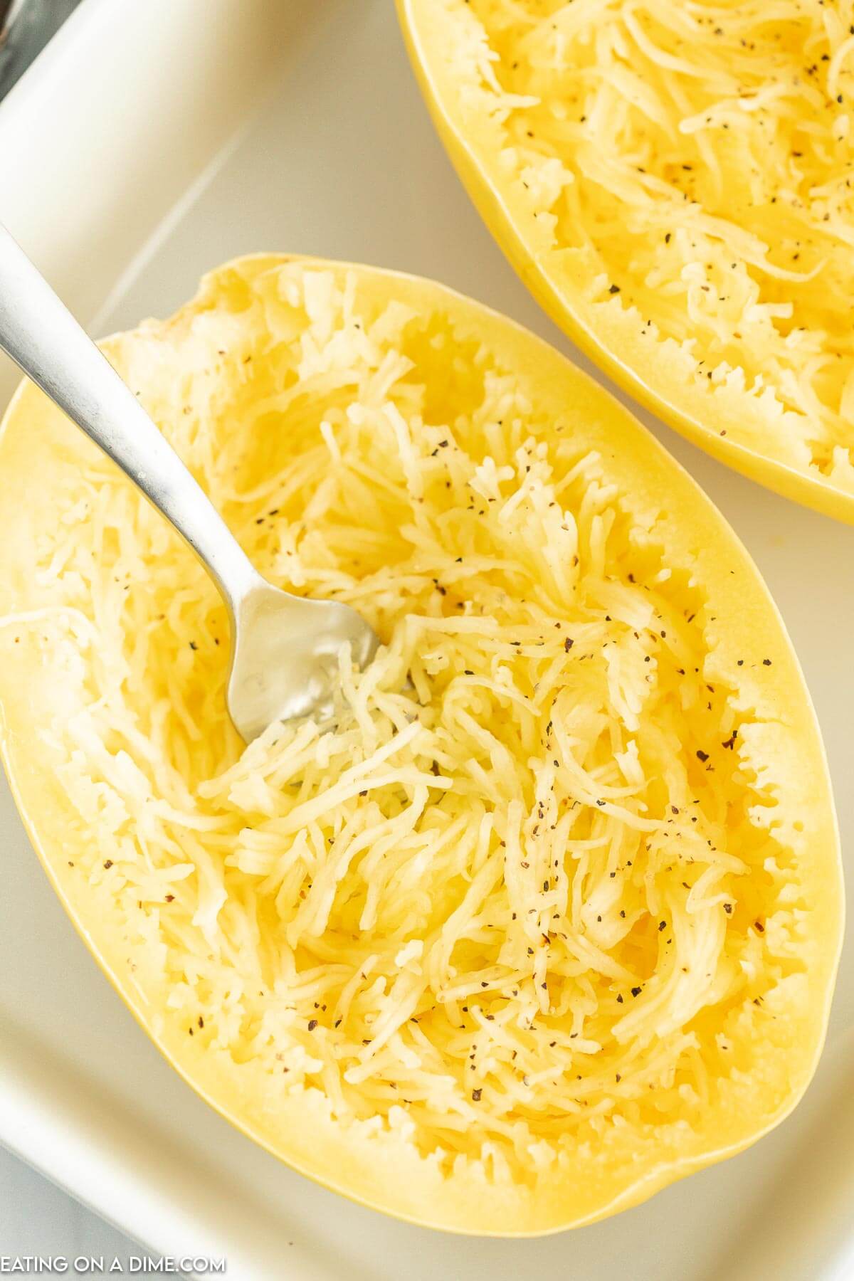 Cooked spaghetti squash in a baking dish with a fork shredding the squash