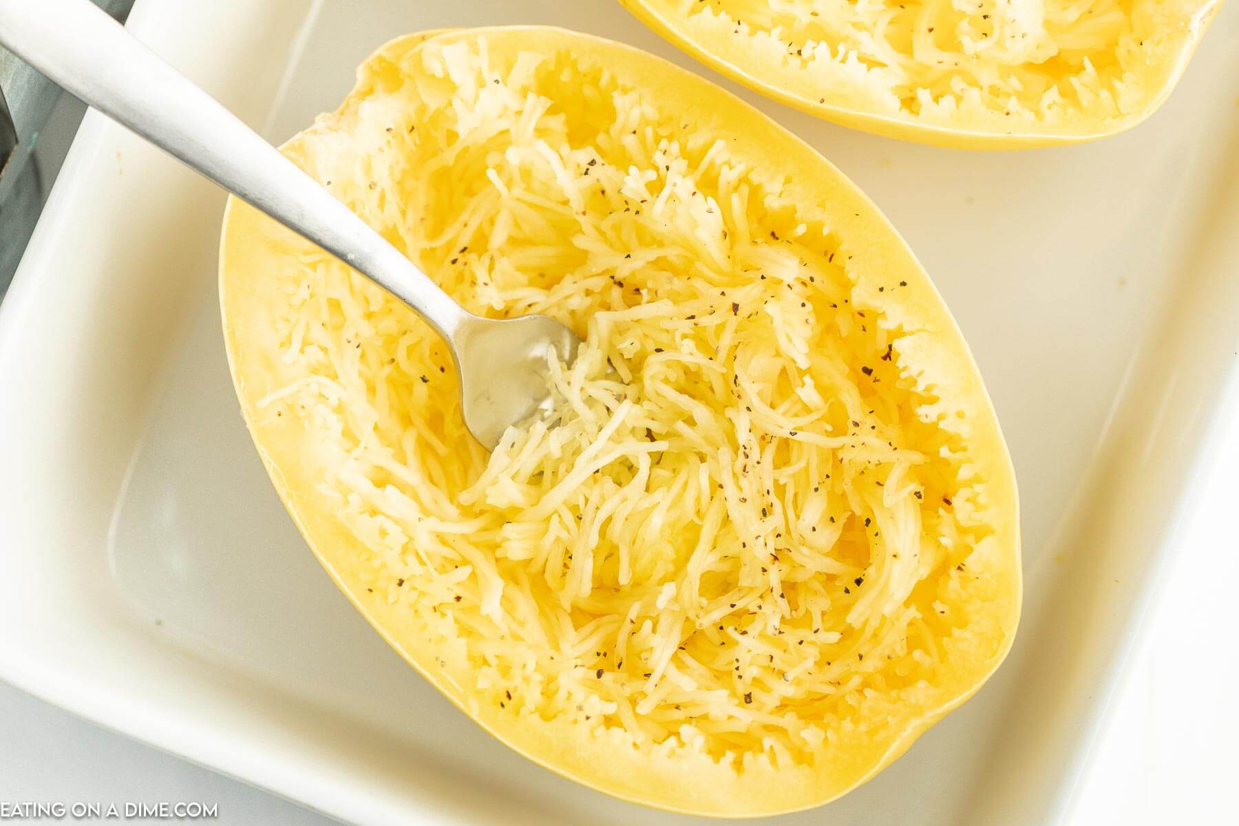 Cooked spaghetti squash in a baking dish with a fork shredding the squash